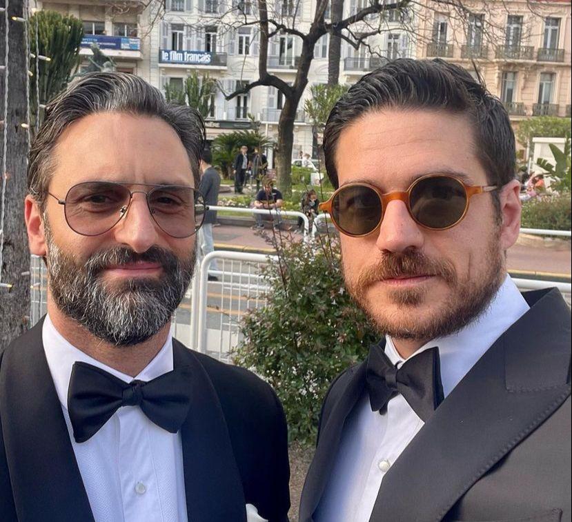Marco Pigossi e Marco Calvani posam para foto. Os dois estão de smoking e usam óculos escuros