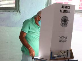 Imagem mostra um eleitor não identificado em uma cabine de votação da Justiça Eleitoral em dia de escolha de novos representantes na política. Trata-se de um homem aparentemente idoso, que usa óculos, máscara de proteção, uma camisa verde água e uma bermuda jeans de lavagem clara.