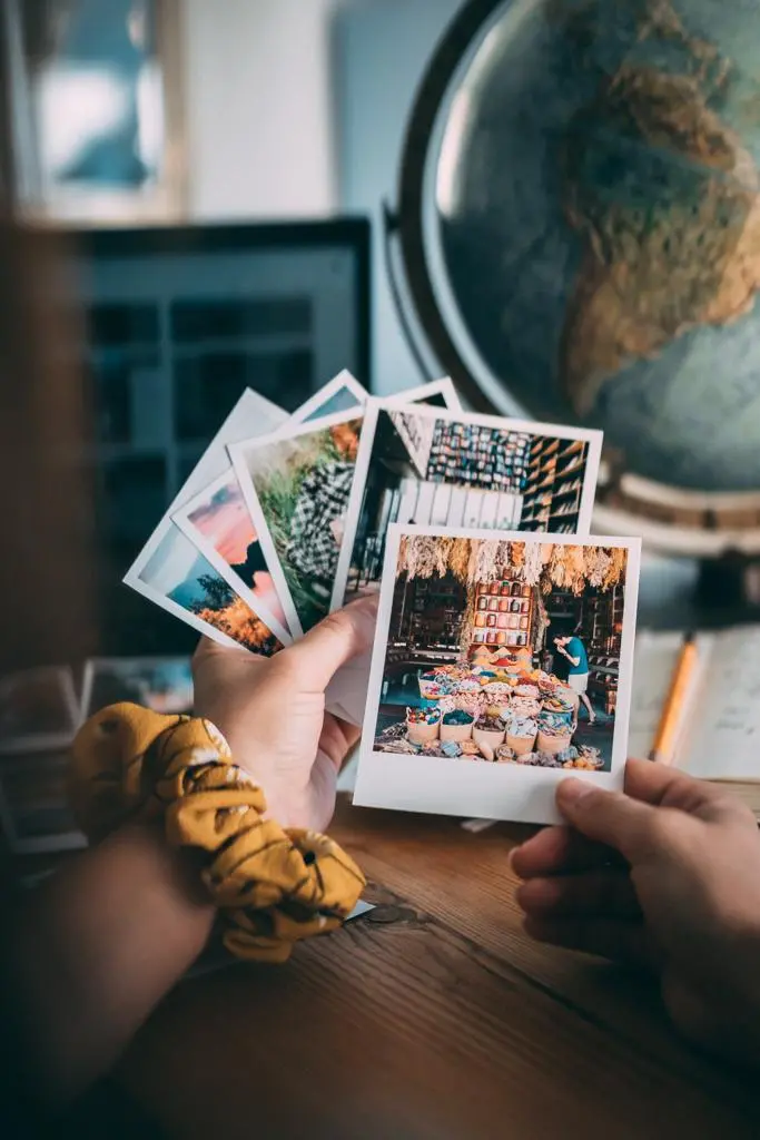 Mão segurando fotos polaroides na frente de um globo