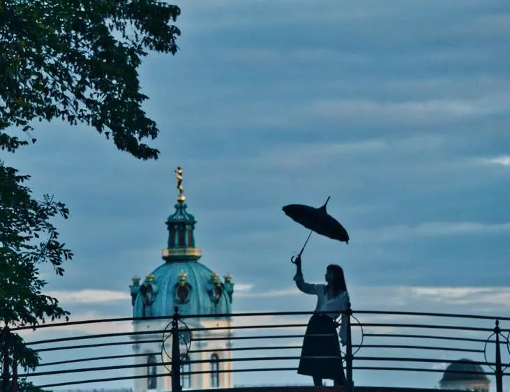 Uma mulher ergue um guarda-chuva com um dos braços enquanto anda em cima de uma ponte