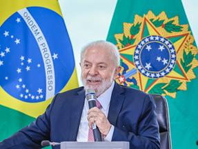 Presidente Lula segura microfone enquanto discursa em frente à bandeira do Brasil