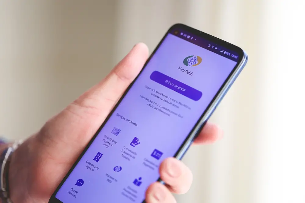 Mão segurando celular com aplicativo do INSS