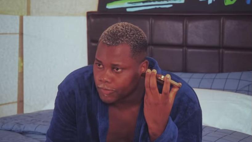 MC Saci é um homem negro de cabelo curto descolorido e, na foto, está de roupão azul ouvindo áudio no celular