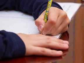 Close-up em mão da criança escrevendo no papel, escrevendo matemática bagunçada na mesa de madeira na sala, estudante segurando caneta fazendo lição de casa em casa, calcule os resultados no papel, conceito de educação.