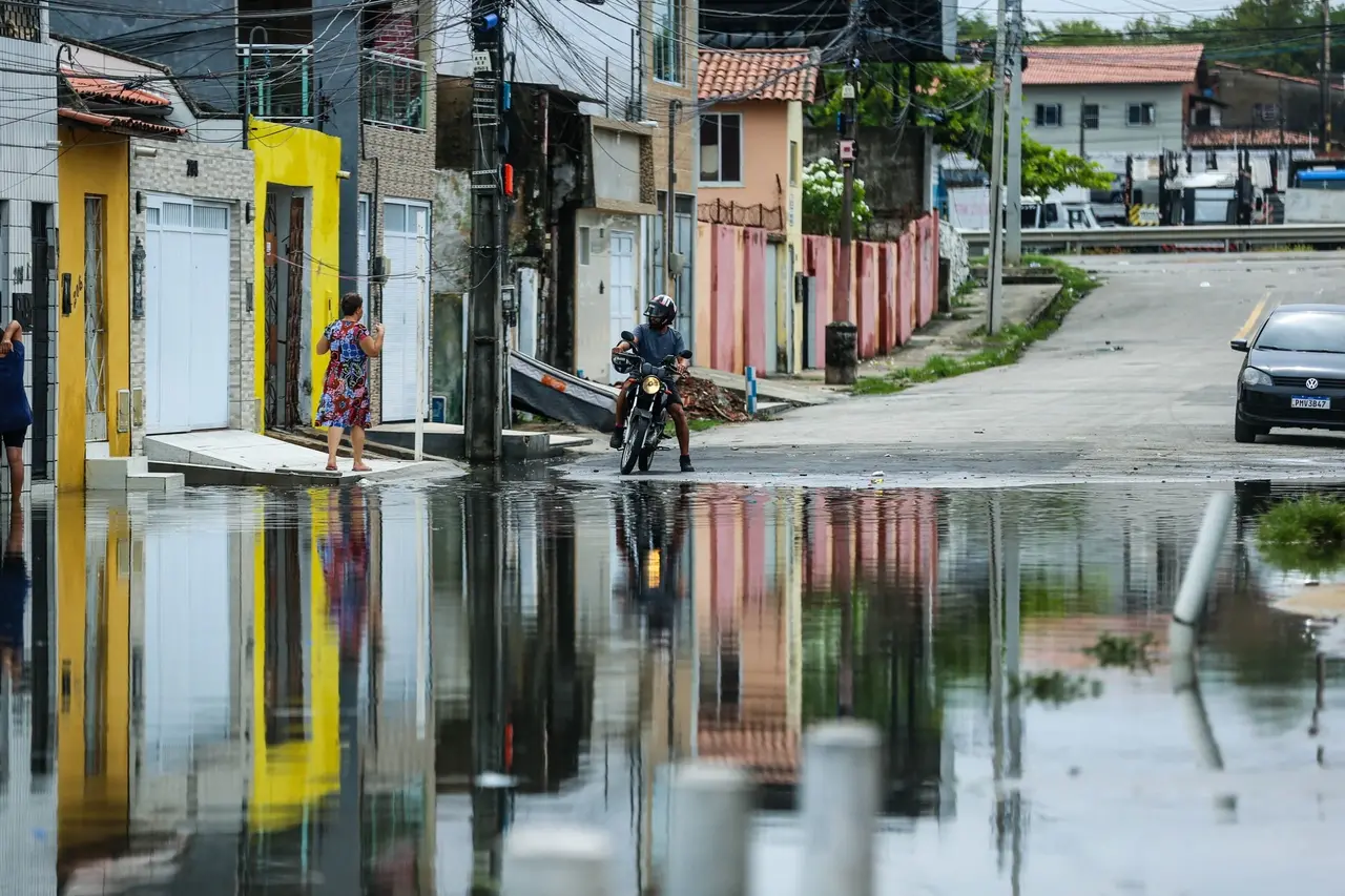 Homem em cima de uma moto observa rua alagada
