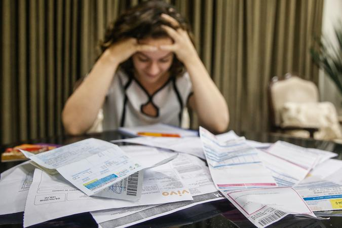 Mulher preocupada diante de mesa com muitas faturas