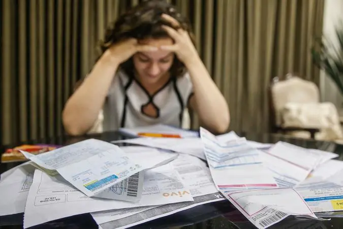 Mulher preocupada diante de mesa com muitas faturas