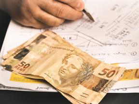 Mão fazendo cálculo com notas de R$ 50