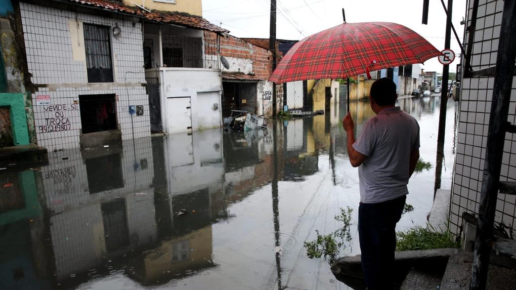 Homem com guarda-chuva observa rua alagada em Fortaleza