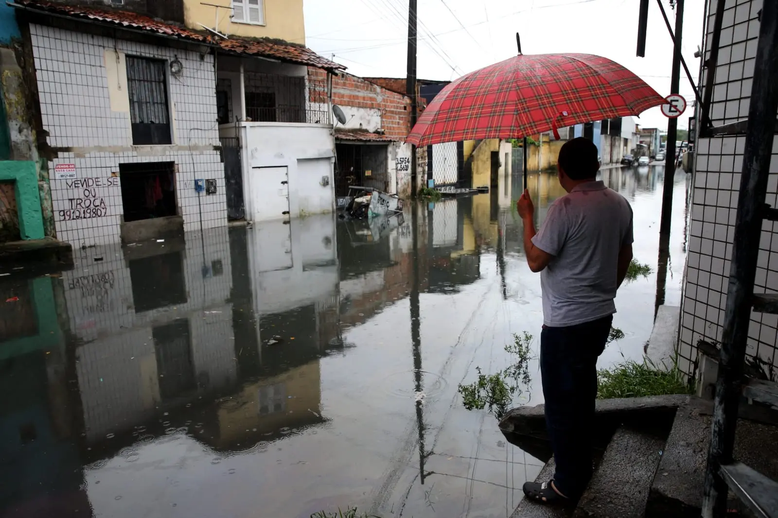 Homem com guarda-chuva observa rua alagada em Fortaleza
