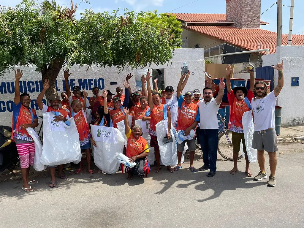 Catadores posam para a foto sorrindo e levantando os braços, junto de grandes sacolas plásticas brancas