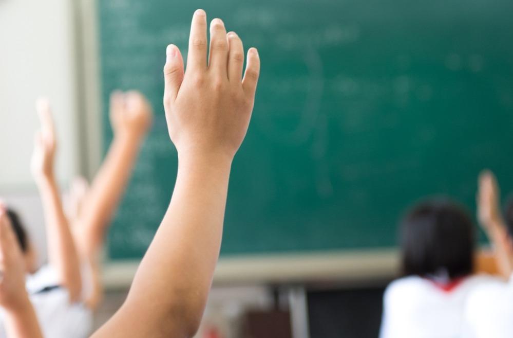 Mão de criança levantando em sala de aula em frente a lousa