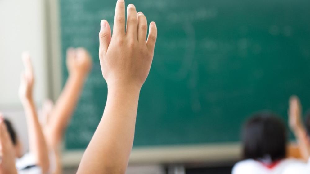 Mão de criança levantando em sala de aula em frente a lousa