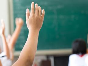 Mão de criança levantando em sala de aula em frente a lousa