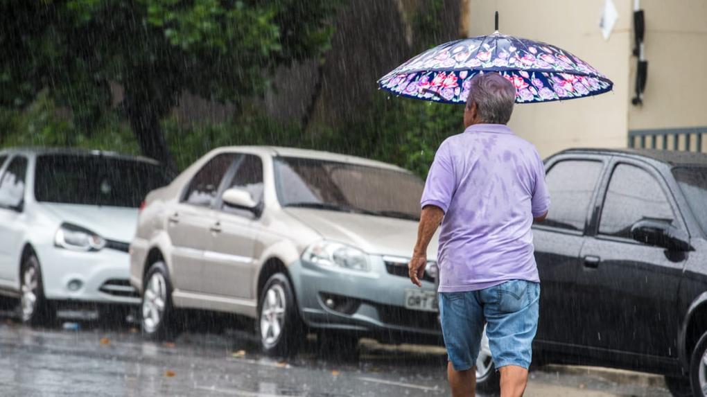 Homem atravessa a rua com guarda-chuvas