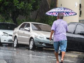 Homem atravessa a rua com guarda-chuvas