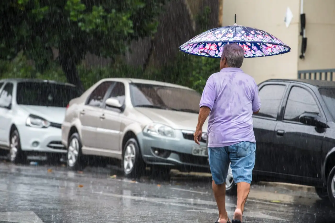 Homem atravessa a rua com guarda-chuvas