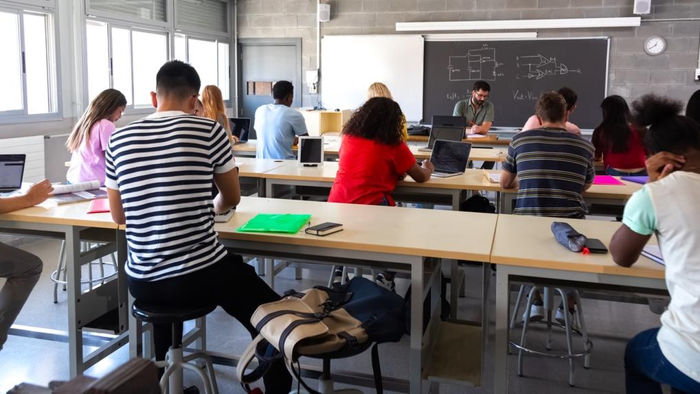 Vista traseira de um grupo de estudantes multirraciais do ensino médio em sala de aula usando laptops enquanto o professor marca os exames. Inscrições para o Fies começam nesta terça-feira (12); saiba como participar