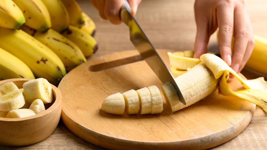 pessoa partindo banana com cacho de bananas ao fundo