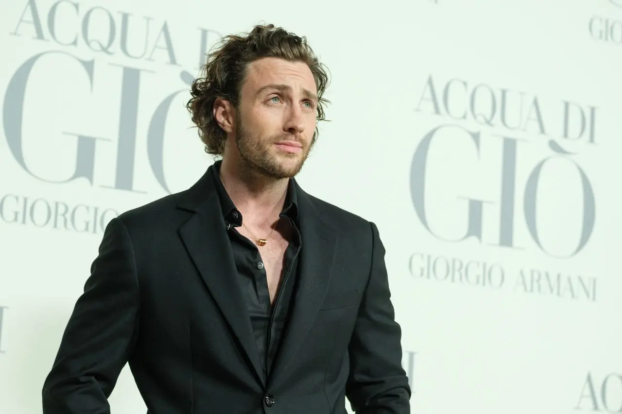 Aaron Taylor-Johnson vestindo terno preto diante de painel com o nome acqua di gio