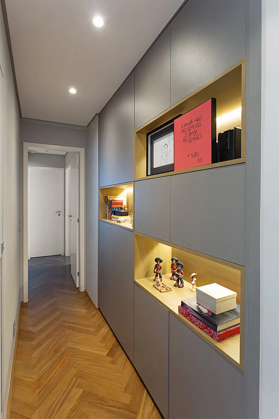 O corredor encaminha ao closet dos moradores. Ela propôs a remoção da parede que separava o espaço com o closet e ocupou o lugar com a marcenaria com armários e nichos
