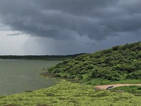 Vista do Açude Banabuiú, com vegetação verde ao redor e nuvens escuras no céu