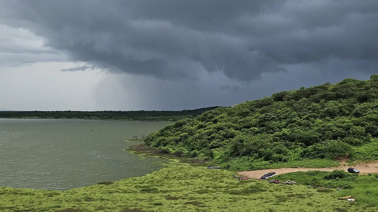 Vista do Açude Banabuiú, com vegetação verde ao redor e nuvens escuras no céu