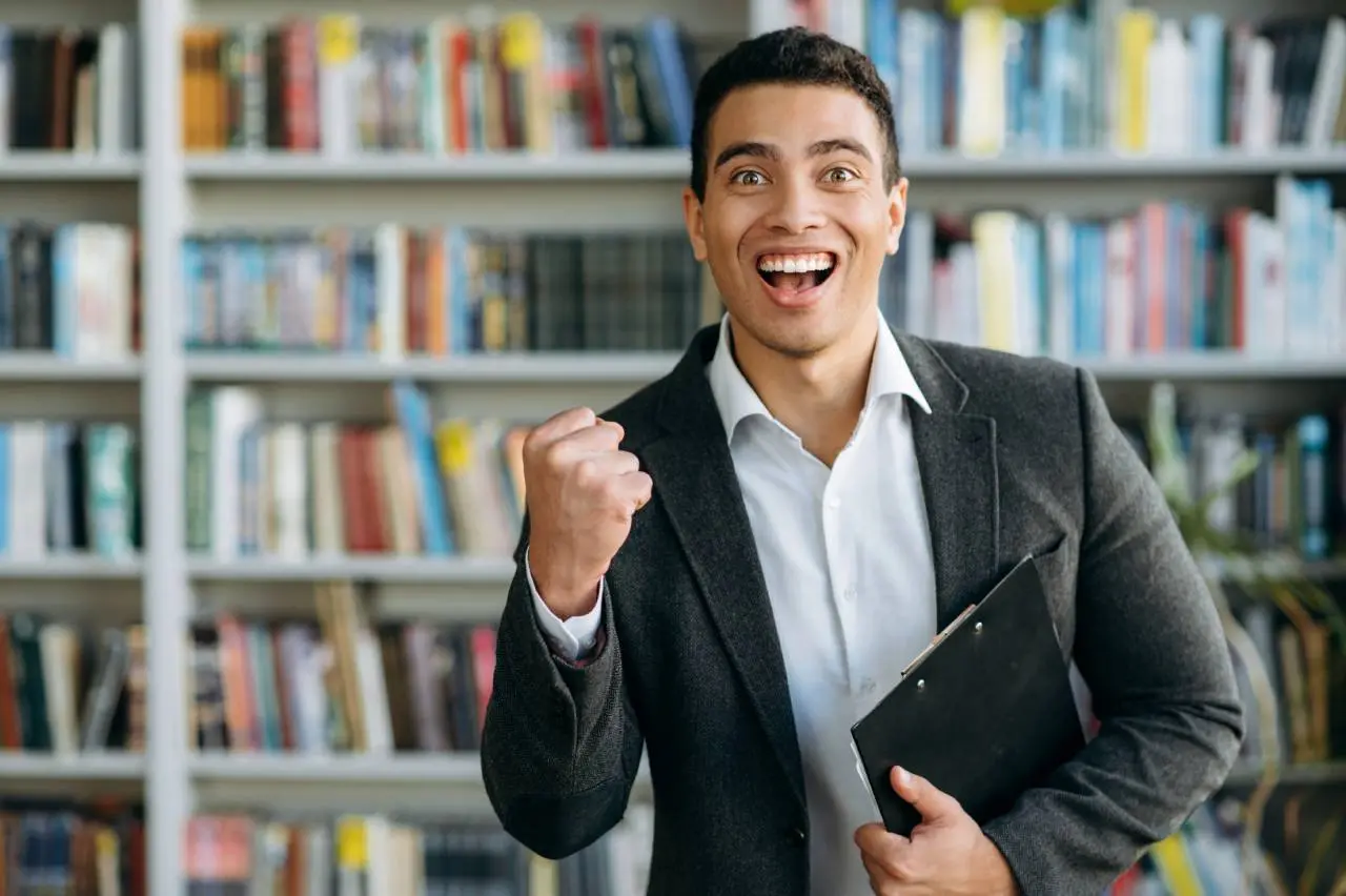 Homem jovem de terno comemora segurando uma prancheta