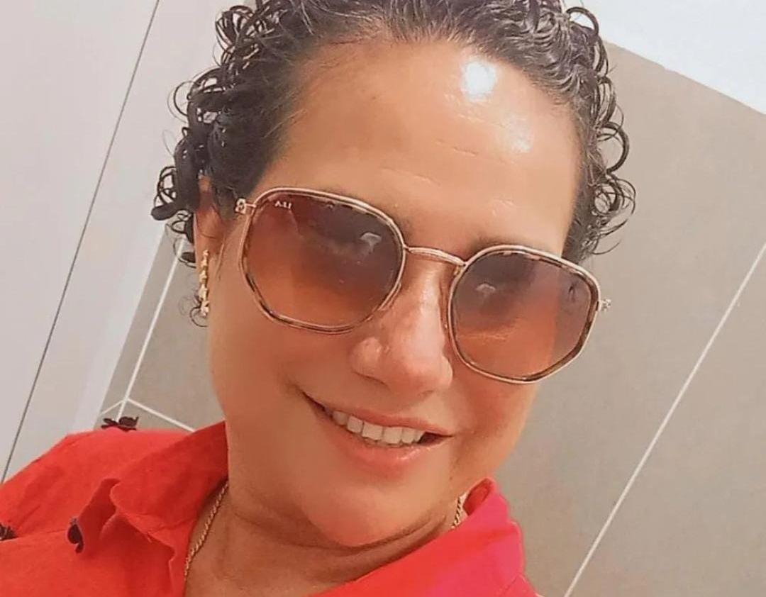 Selfie de professora. Ela tem cabelos enrolados, curtos, e está de óculos escuros na foto