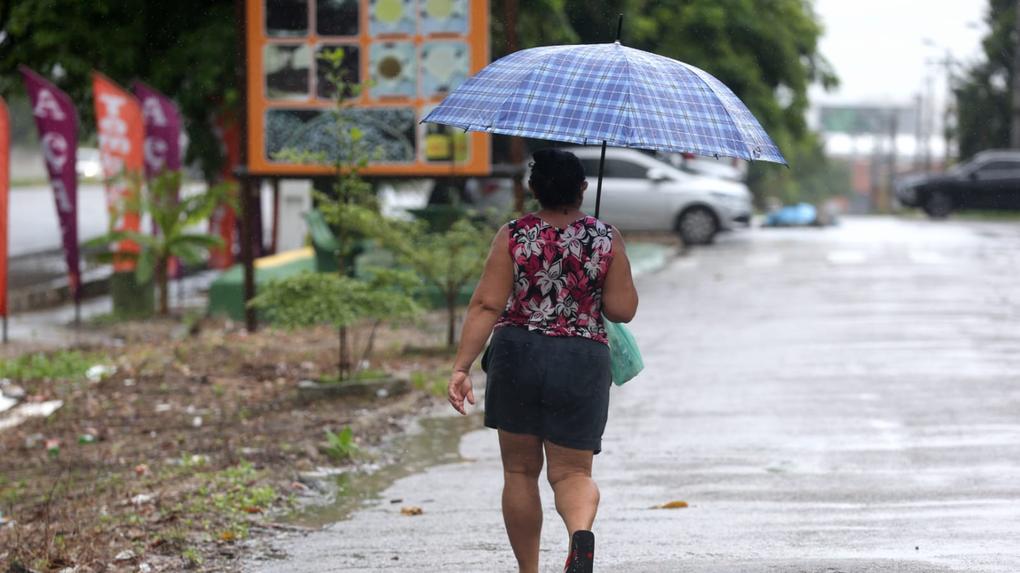 Mulher caminha por rua segurando guarda-chuva