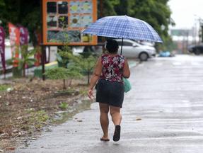 Mulher caminha por rua segurando guarda-chuva