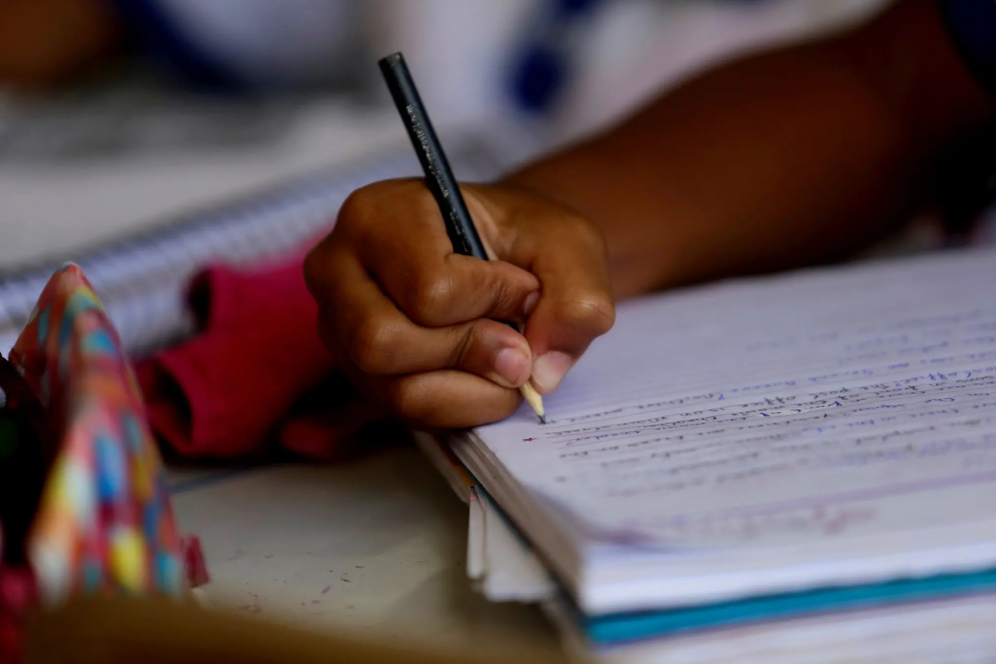 Mão de criança negra escrevendo com lápis em um caderno