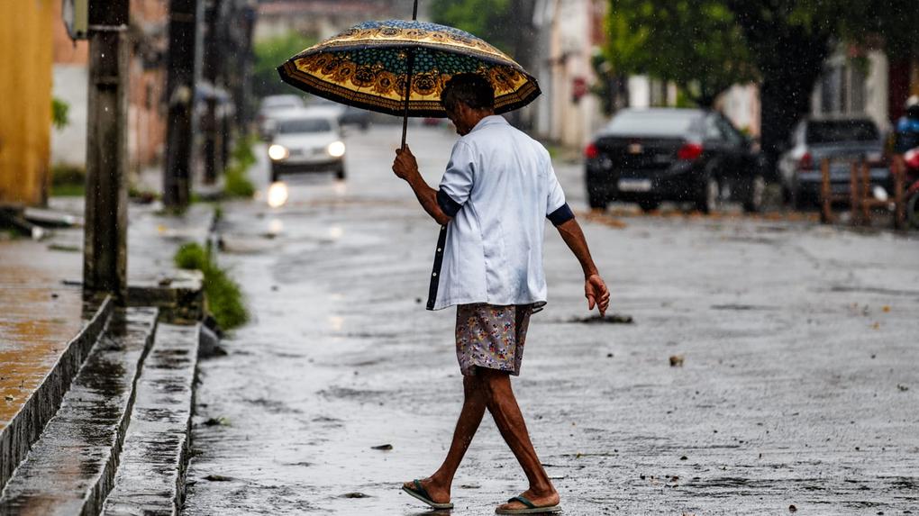 Homem anda em rua de Fortaleza com guarda-chuvas