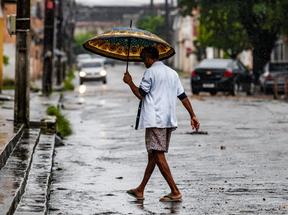 Homem anda em rua de Fortaleza com guarda-chuvas