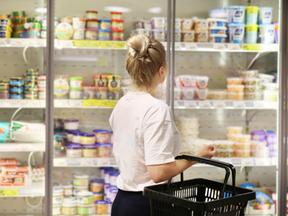 Mulher branca e loira observa de costas produtos lácteos no supermercado