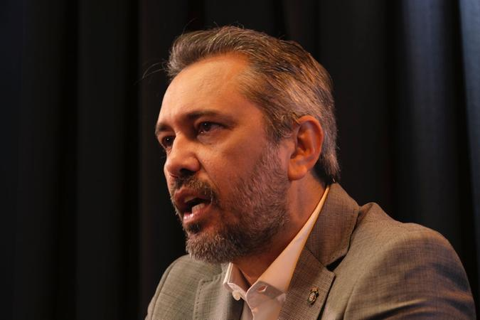 O governador Elmano é um homem pardo com cabelos e barbas grisalhos. Ele está falando em um estúdio de podcast