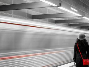 Imagem de mulher de bolsa vermelha em frente a um metrô veloz