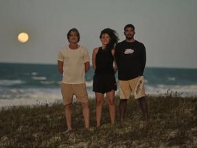 Os atores Fábio Assunção, Nataly Rocha e Iago Xavier posam para foto em praia com lua ao fundo