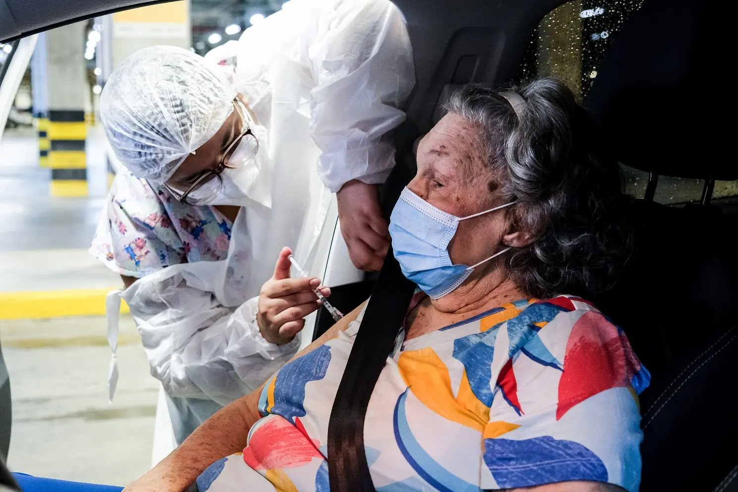 Idosa recebe reforço da vacina contra a Covid-19 dentro de um carro