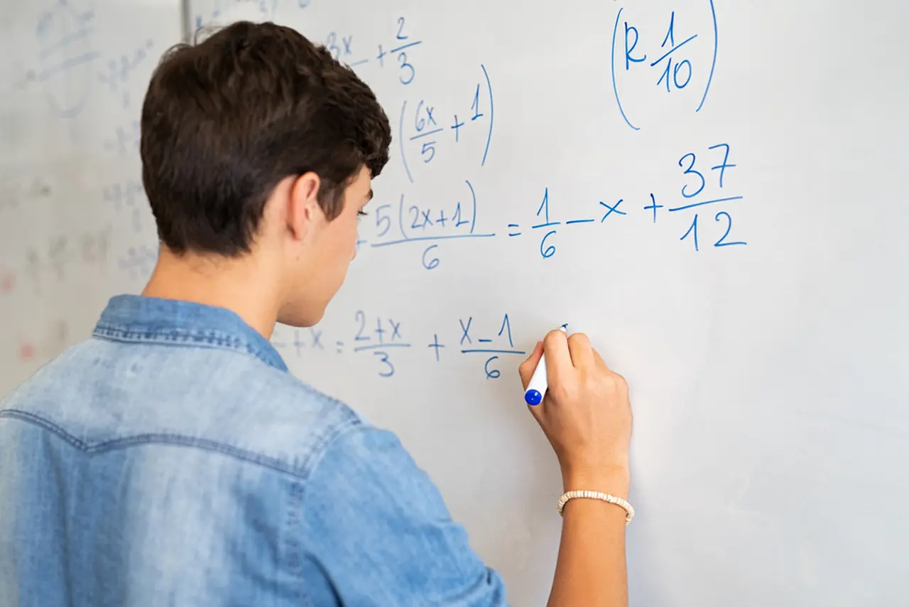 Estudante escreve fórmulas matemáticas na lousa
