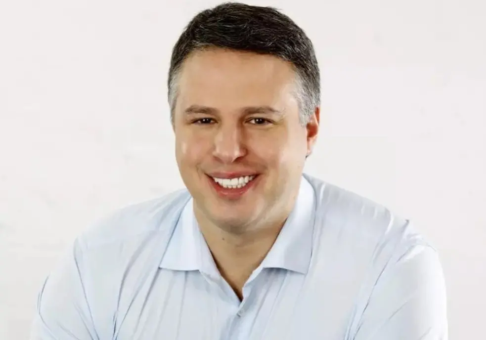 Arthur Bisneto é um homem branco de cabelo grisalho aos lados. Na foto, ele está sorrindo e usa camisa azul clara