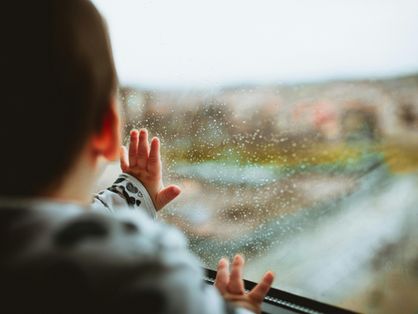 Criança de costas olhando por uma janela de vidro