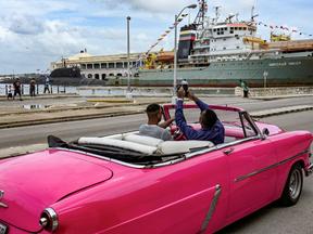 pessoas em carro rosa fotografando embarcações russas em cuba