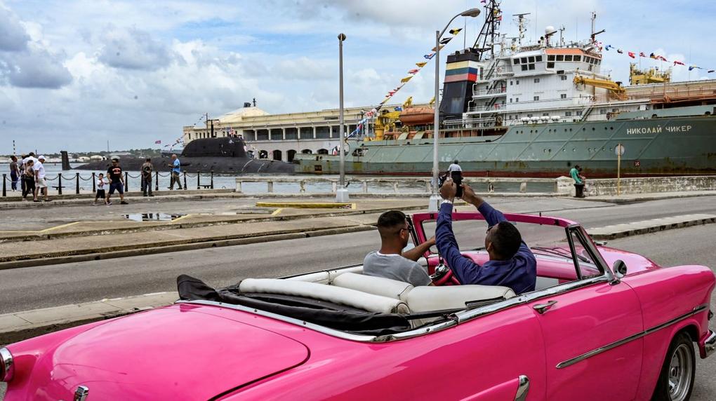 pessoas em carro rosa fotografando embarcações russas em cuba