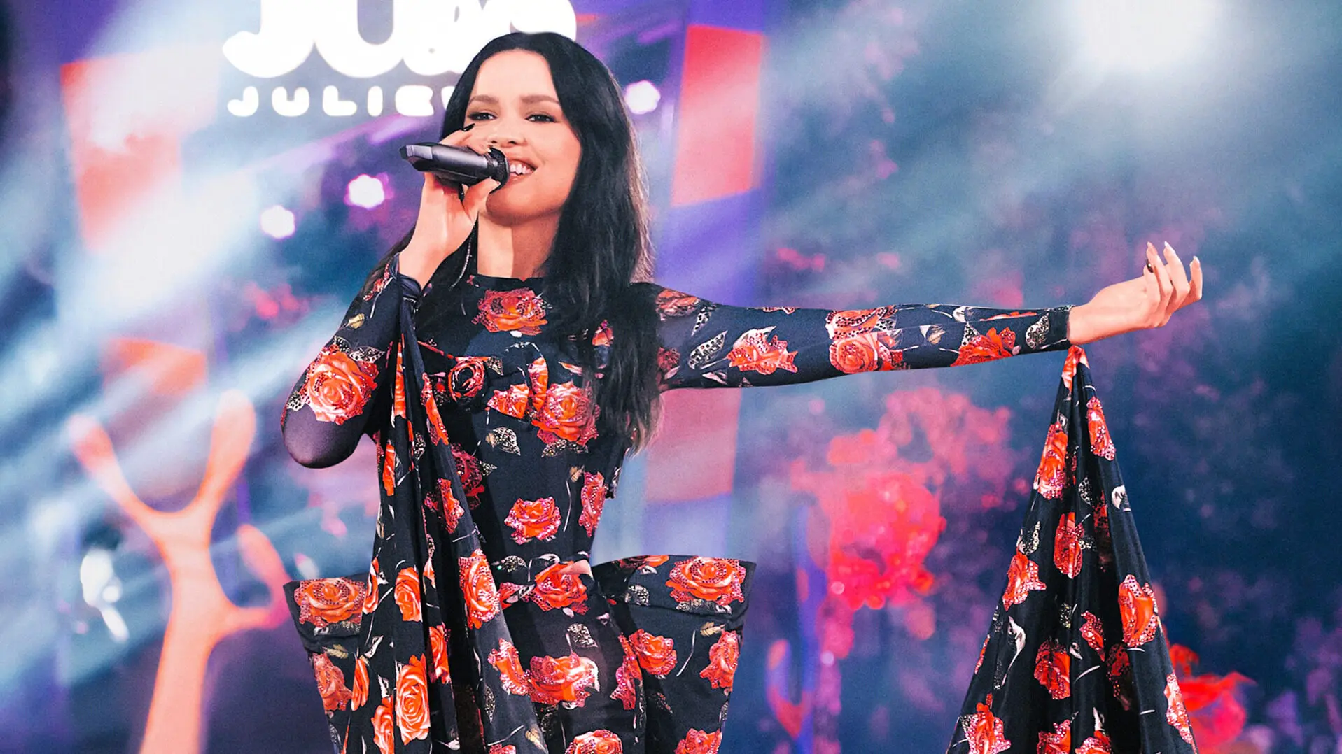 Cantora Juliette com microfone e vestido floral em preto e vermelho