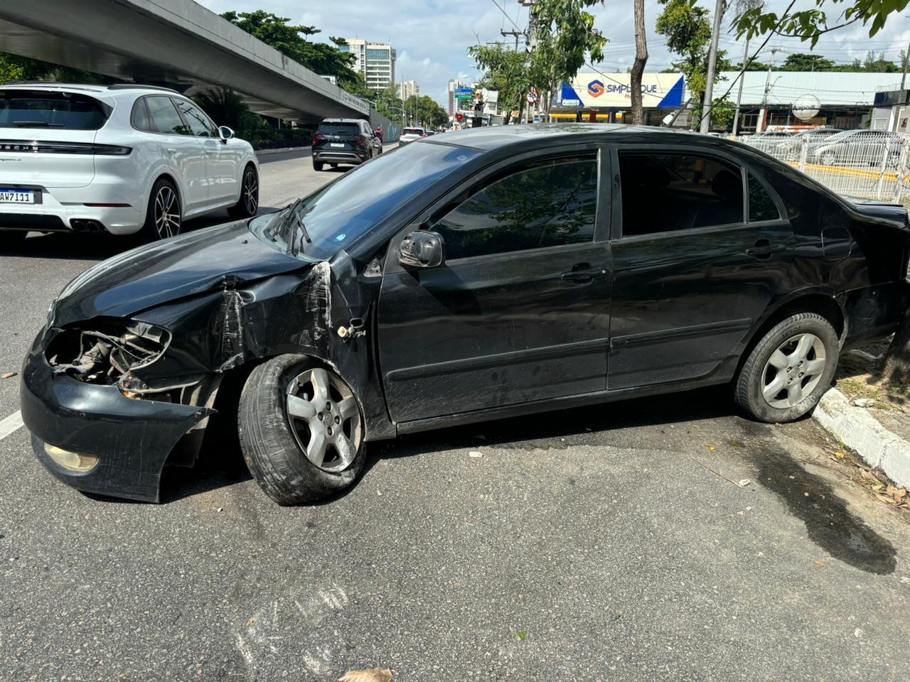 Carro preto sedan amassado após batida em poste de energia