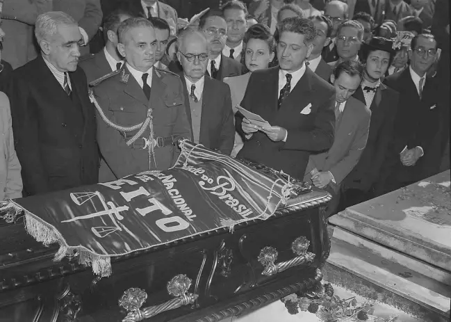 Imagem em preto e branco do funeral de Clóvis Bevilaqua. Na imagem, vários homens estão ao redor do caixão do jurista