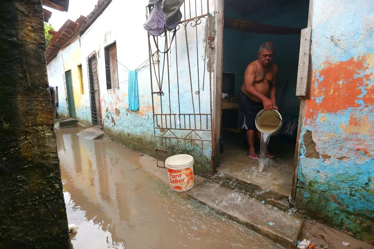 Homem tira água de casa com balde após inundação em Caucaia, no Ceará