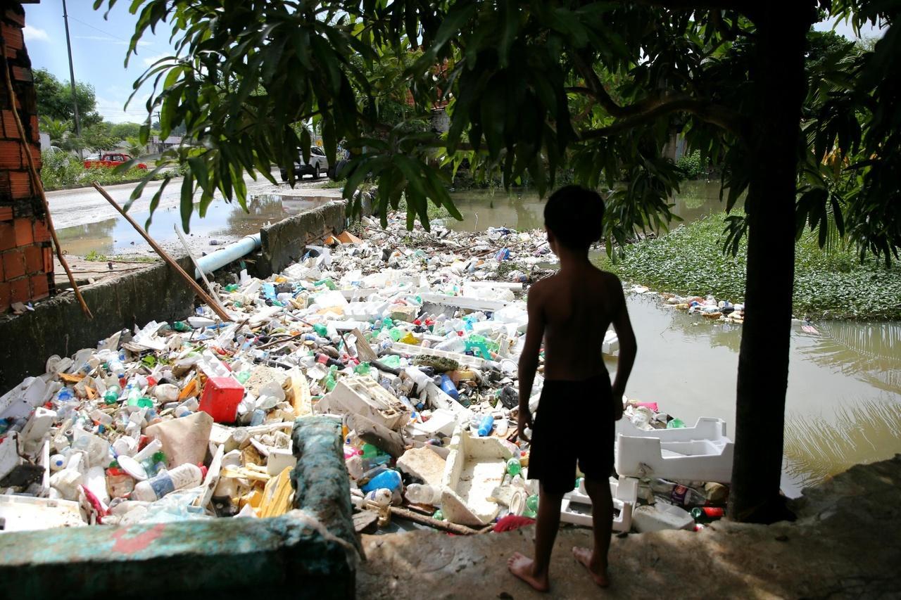 Menino olha para rio tomado por lixo em Caucaia, no Ceará