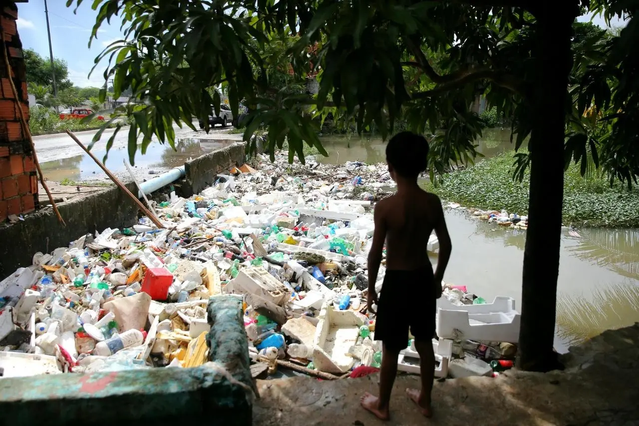 Menino olha para rio tomado por lixo em Caucaia, no Ceará